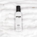PUR HAIR Style Dry Foam Shampoo – weiße Flasche mit schwarzem Deckel, liegend auf fluffigem Schaum
