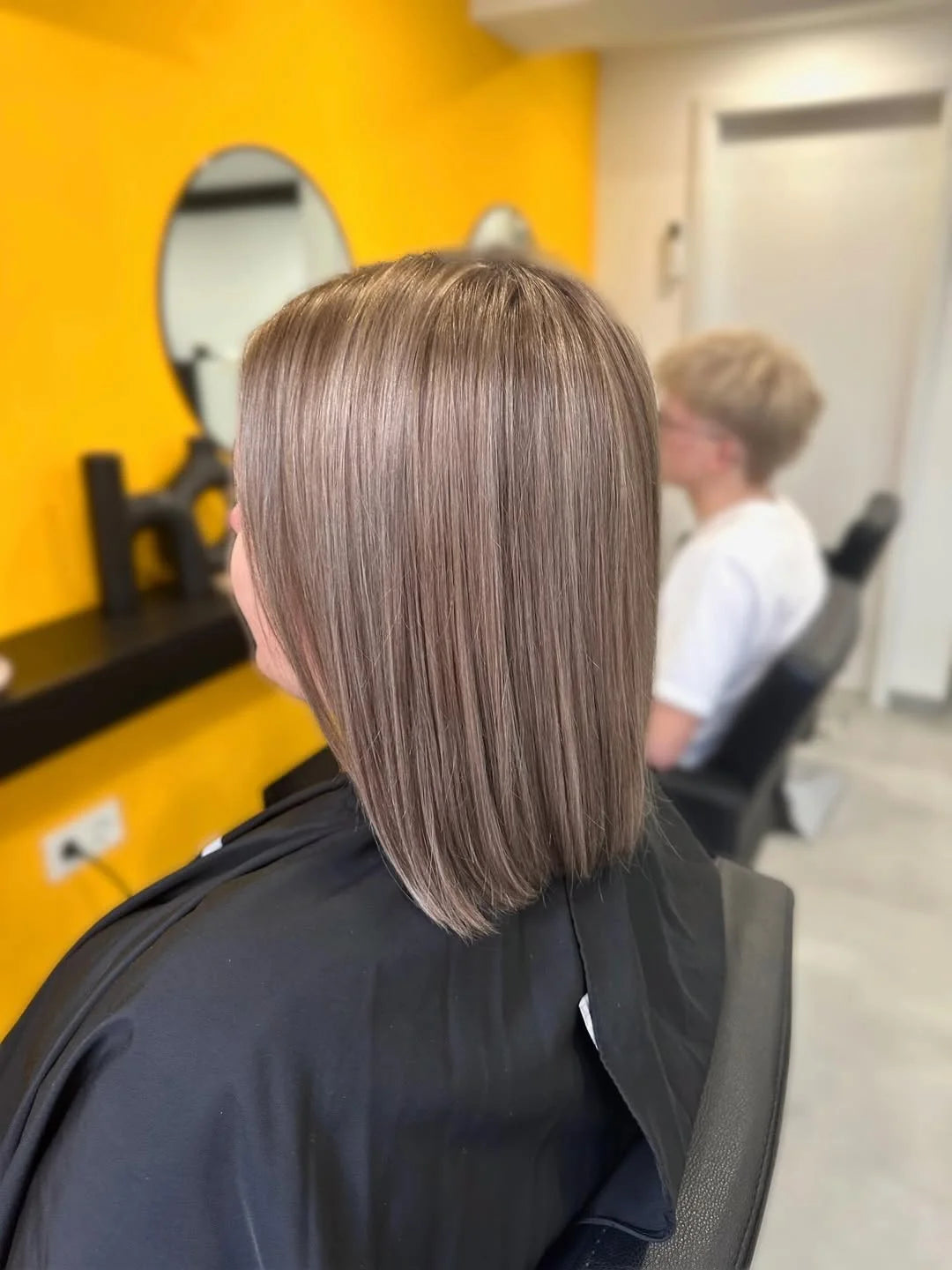 Haarmodel vor orangenem Hintergrund mit Schulterlangen gepflegten glatten dunkelblondem Haar.