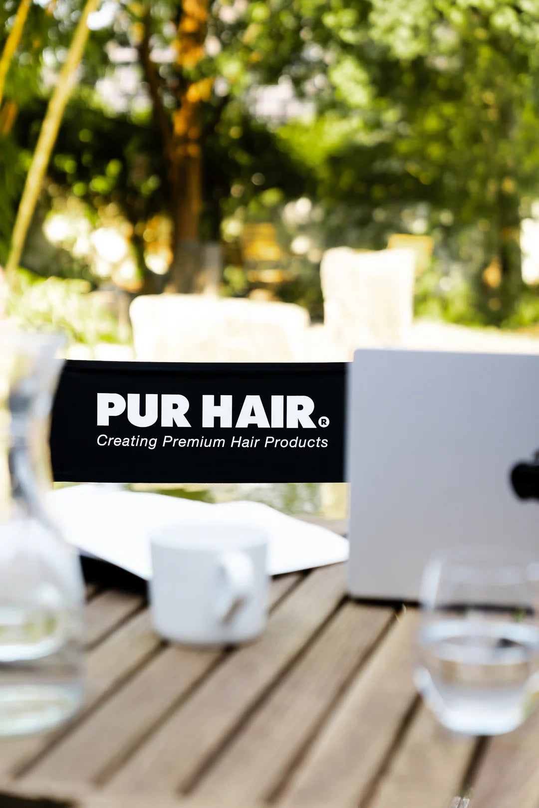 PUR HAIR Arbeitsplatz im Freien mit Laptop, Unterlagen und Logo „Creating Premium Hair Products“.
