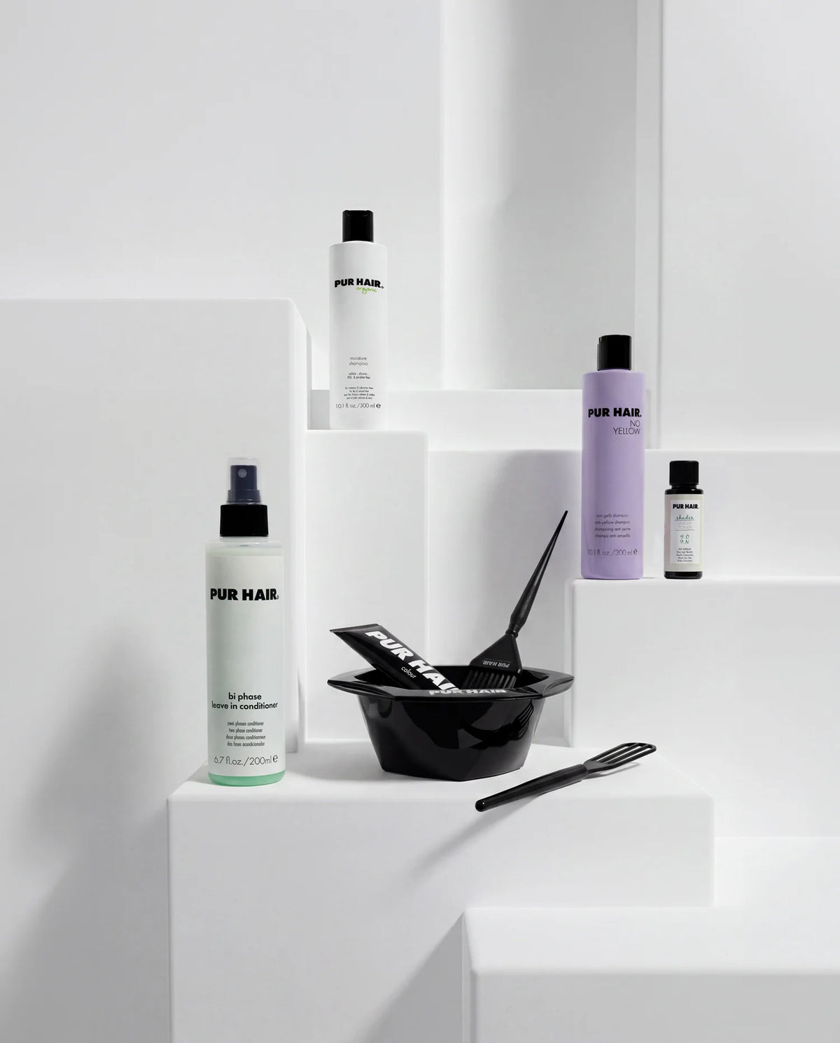 Auswahl verschiedener PUR HAIR Haarpflege-, Farb- und Salonzubehör-Produkte auf weißen Podesten im minimalistischen Studio.