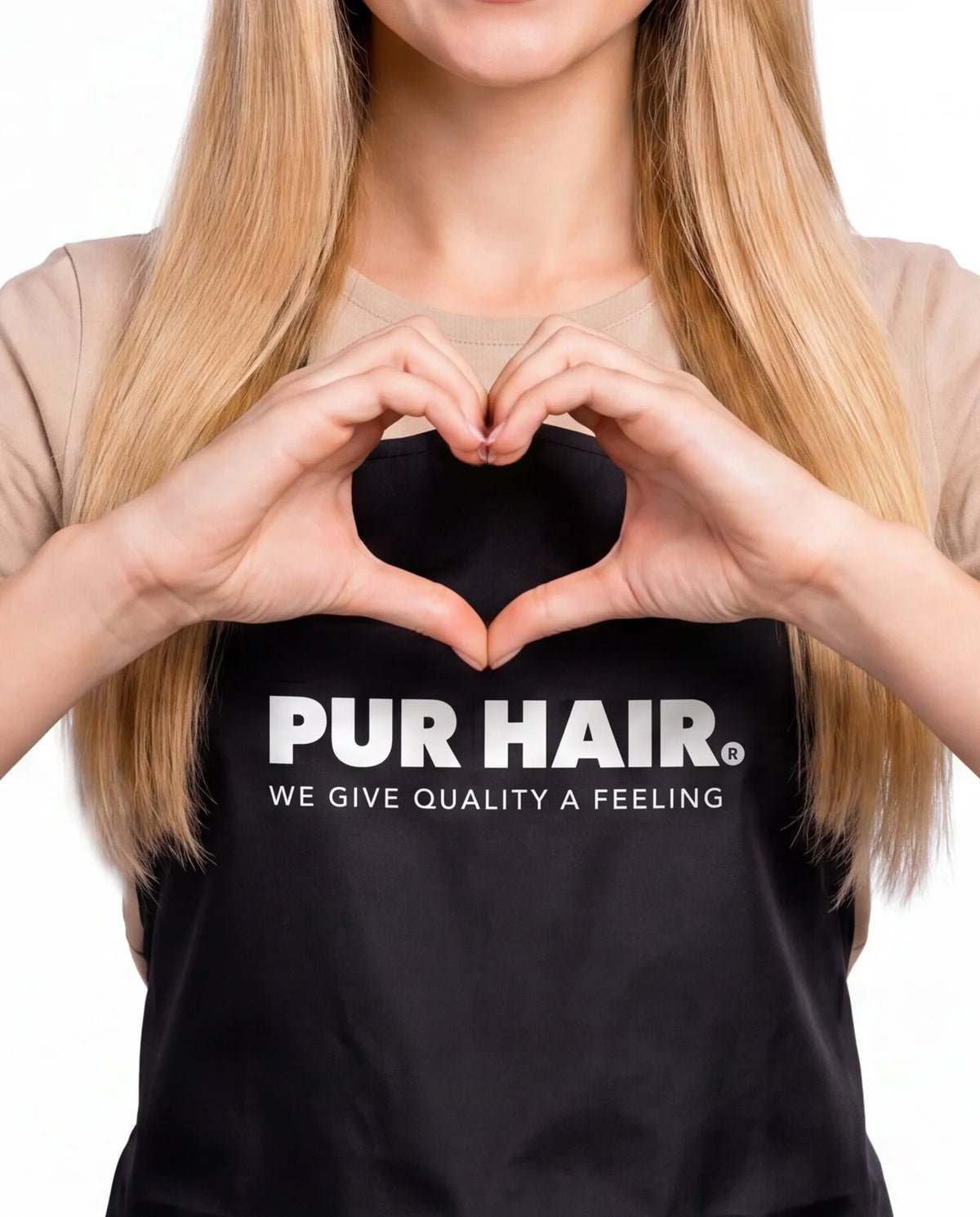 Friseurin mit langen blonden Haaren und PUR HAIR Schürze formt mit ihren Händen ein Herz.