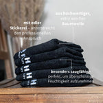 Stapel schwarzer PUR HAIR Baumwollhandtücher auf einer Holzablage mit weißer Stickerei und Hinweisen