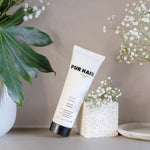 PUR HAIR Organic Moisture Treatment steht angelehnt an einem weißen Steinblock, dokoriert mit Blumen