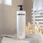 Weiße Flasche PUR HAIR Organic Reconstructor, 1000 ml, auf grauem Handtuch im Bad.