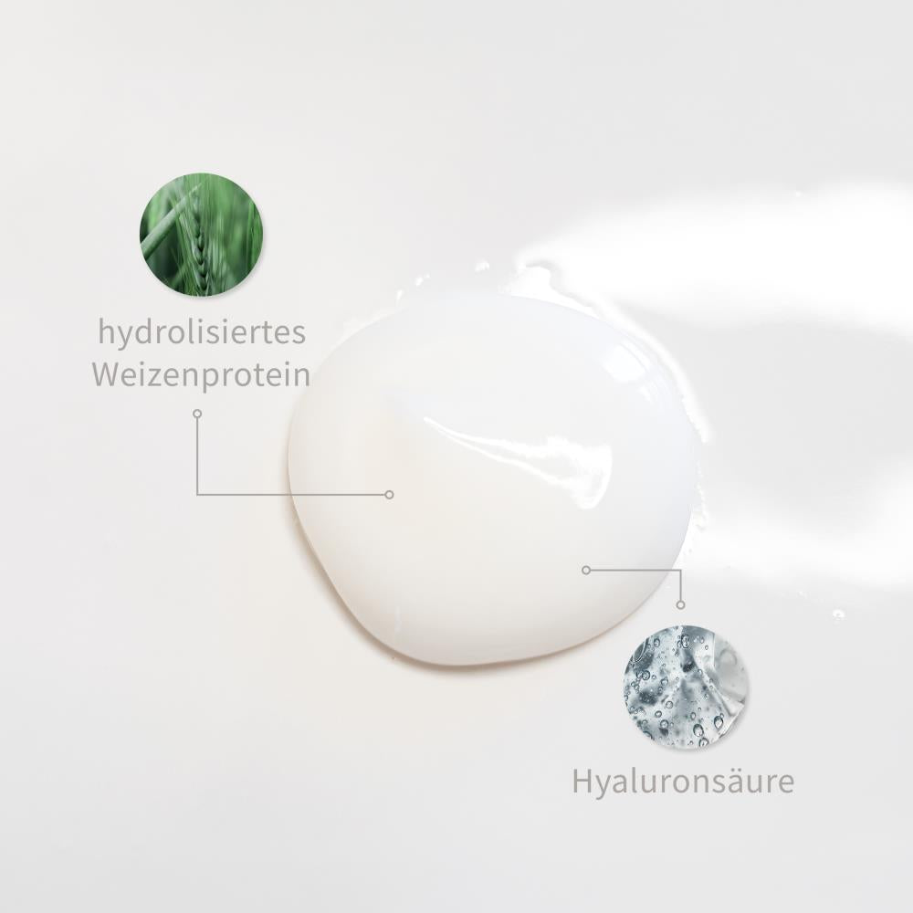 Weiße Creme-Textur mit markierten Inhaltsstoffen: Hydrolysiertes Weizenprotein, Hyaluronsäure.
