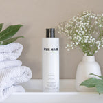 Weiße Flasche PUR HAIR Organic Volume Shampoo, 300 ml, neben grauen Handtüchern mit  Trockenblumen