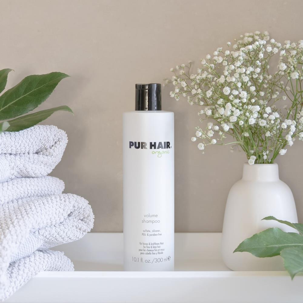 Weiße Flasche PUR HAIR Organic Volume Shampoo, 300 ml, neben grauen Handtüchern mit  Trockenblumen